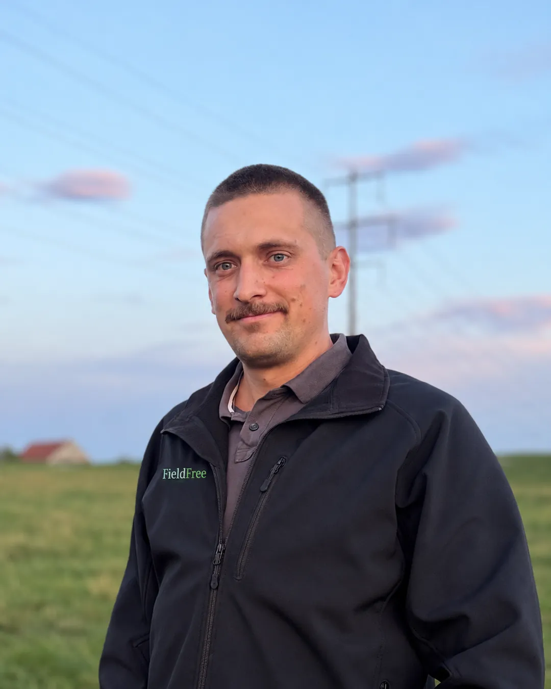 Pascal Ott in seiner FieldFree-Jacke auf einer Wiese in Märwil, im Hintergrund Abendhimmel und ein Bauernhaus